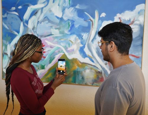 Joyce and Nitish demonstrate the app on a smartphone while standing in front of a painting in a museum.