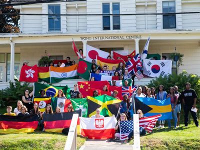 Dozens of students stand in front of the Wong International Centre, holding flags of several nations.