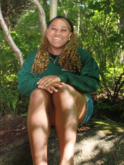 Angel Percentie smiles while sitting in a forest on a warm day.