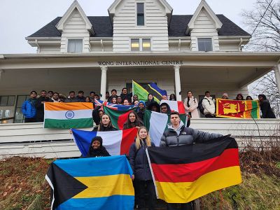 Dozens of students stand in front of the Wong International Centre, holding flags of several nations.