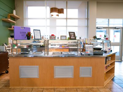 The updated dining station in bright, windowed space in Wheelock Dining Hall: a large area of wooden cabinets with stainless steel countertops and appliances.