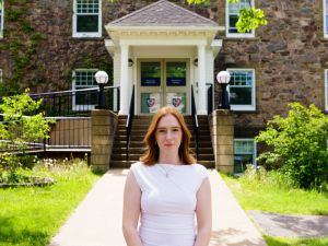 Sophia stands in front of Acadia's Horton Hall on a sunny day while wearing a professional white dress.
