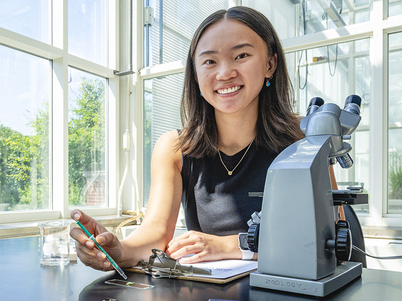 A female student smiles while working with a microscope in the K.C. Irving Environmental Science Centre