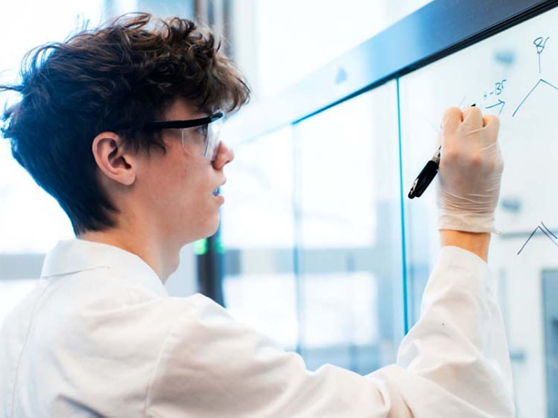 A male student draws a chemistry diagram on a glass surface