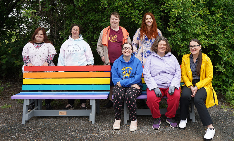 Polly Leonard and Allison Smith smile on the new Pride benches alongside members from the Flower Cart.
