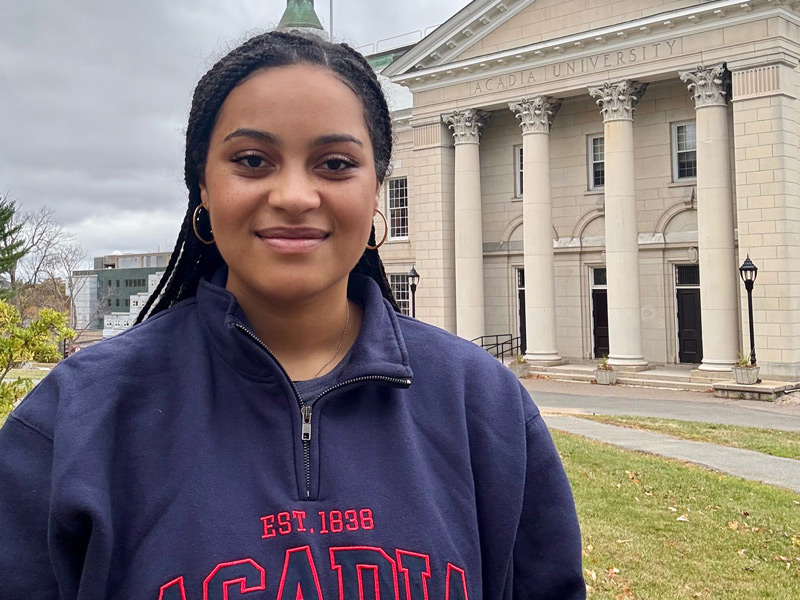 Wellness Champion Michaela Dankwa smiles as she stands in front of University Hall on an autumn day.
