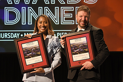 Maya Macatumpag-Murray and Dr. Matthew Corkum smile as they stand on stage with their alumni award plaques at the annual Alumni Dinner event.