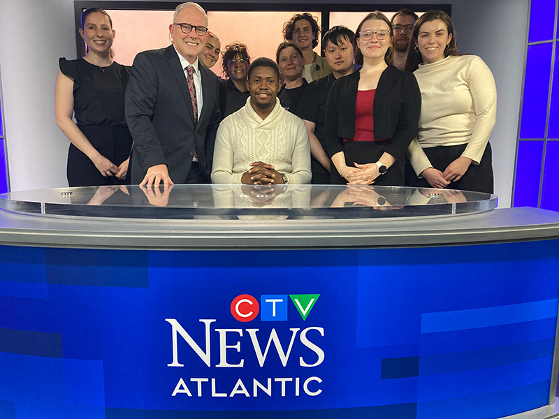 A group of students smiles with CTV broadcasters behind the CTV News Atlantic news desk