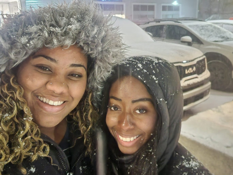 Angel Percentie and a friend smile and huddle together in winter jackets on a stormy winter night in downtown Wolfville.