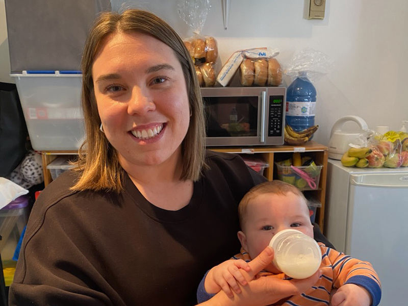 Dr. Jane Francis smiles for the camera while bottle feeding an infant boy in a childcare facility kitchenette area.