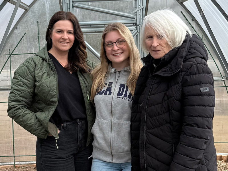 Sea Spray Garden Initiative Board Chair Tracy Milsom, Acadia student Robyn Dearman, and Board Vice-Chair Tracey Smyth stand together in a greenhouse.