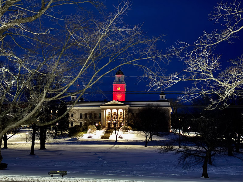University Hall on a winter evening, with the clock tower brightly illuminated by a red floodlight.