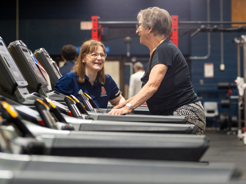 An Acadia trainer and Active for Life participant smile as the participant uses a treadmill in the Fitness Centre