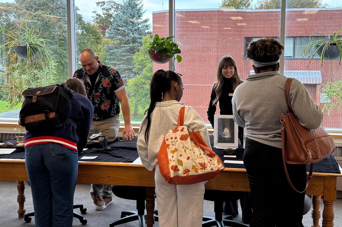 Students review the display tables of archaeological artifacts while Library staff smile.