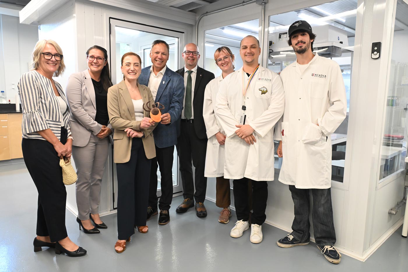 Student researchers pose with federal and provincial officials and Acadia leaders in a brightly lit lab space.