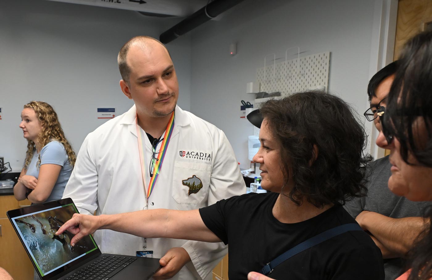 Researchers confer and gesture to a closeup of a tick's anatomy on a laptop screen.