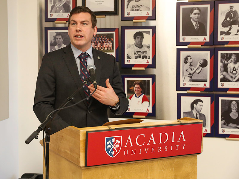 Kody Blois, Member of Parliament for Kings—Hants, speaks from a podium in the Alumni Room in the Acadia Athletics Complex
