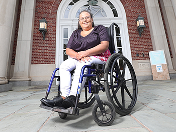 Debra Toney smiles while seated in a wheelchair in front of the KC Irving Centre entrance. Photo credit: Communications Nova Scotia.