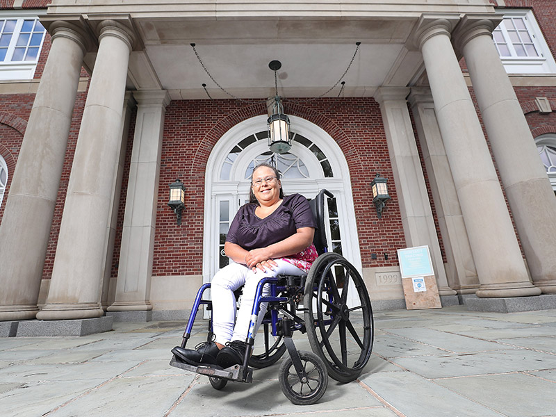 Debra Toney smiles while seated in a wheelchair in front of the KC Irving Centre entrance. Photo courtesy of Communications Nova Scotia.