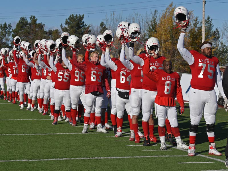 Members of the Acadia Axemen varsity football team line up and hold their helmets in the air in salute