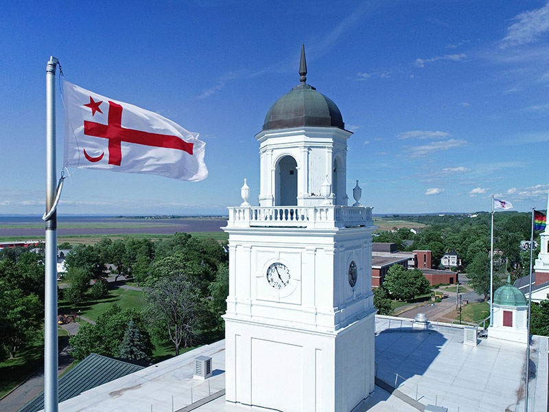 A drone photograph of the Mi'kmaq Grand Council flag flying on a spring day next to the University Hall clock tower.