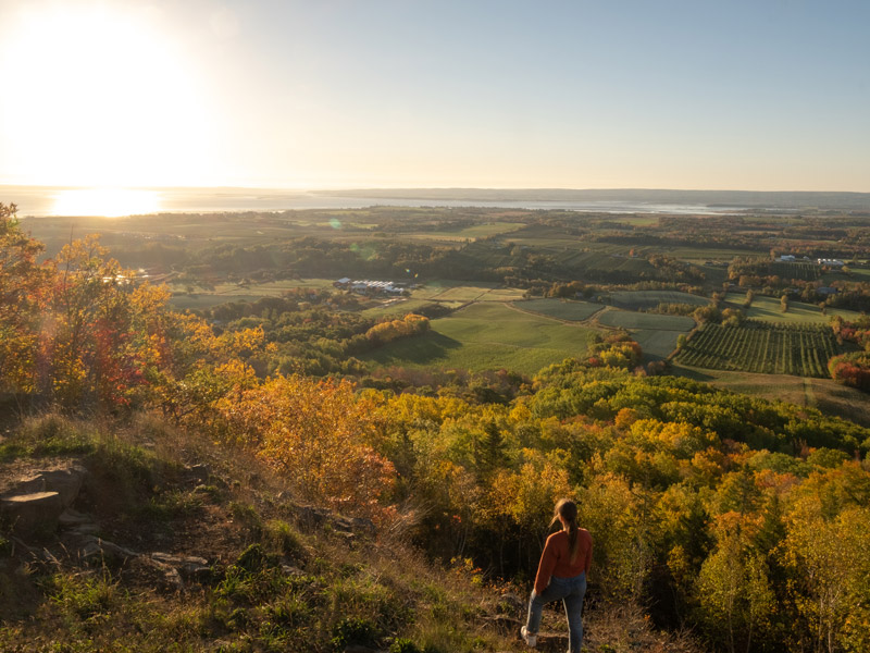 A female student admires the sun rising over the rural farmlands of the Annapolis Valley from the famed Blomidon Lookoff. The fields and foliage are cast in golden glow.