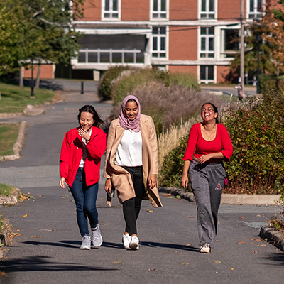 Three female students laugh as they walk uphill from the campus library.