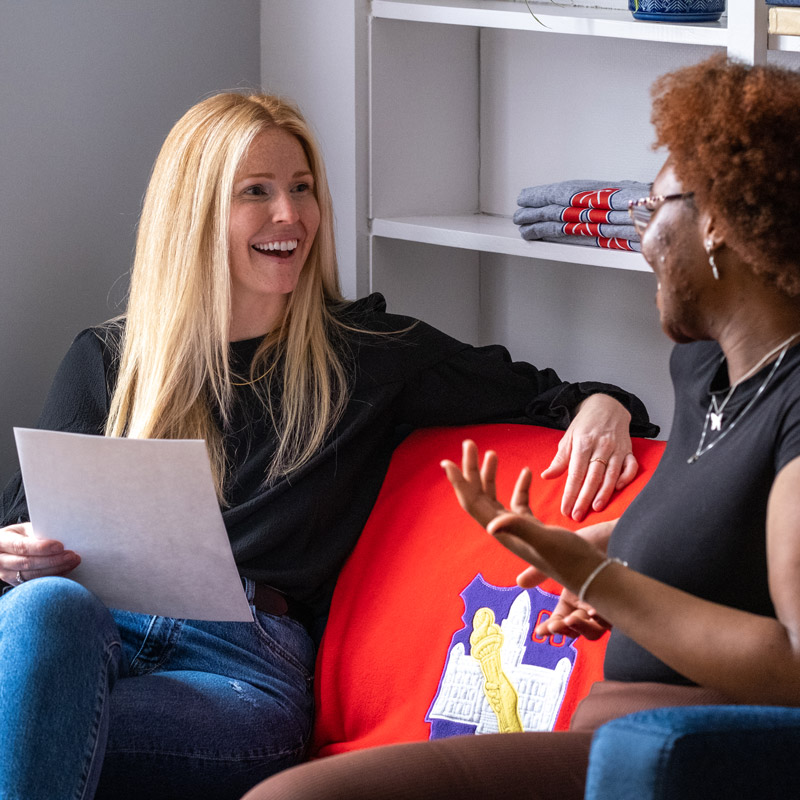 An Acadia staff member and an international student smile as they chat on a couch.