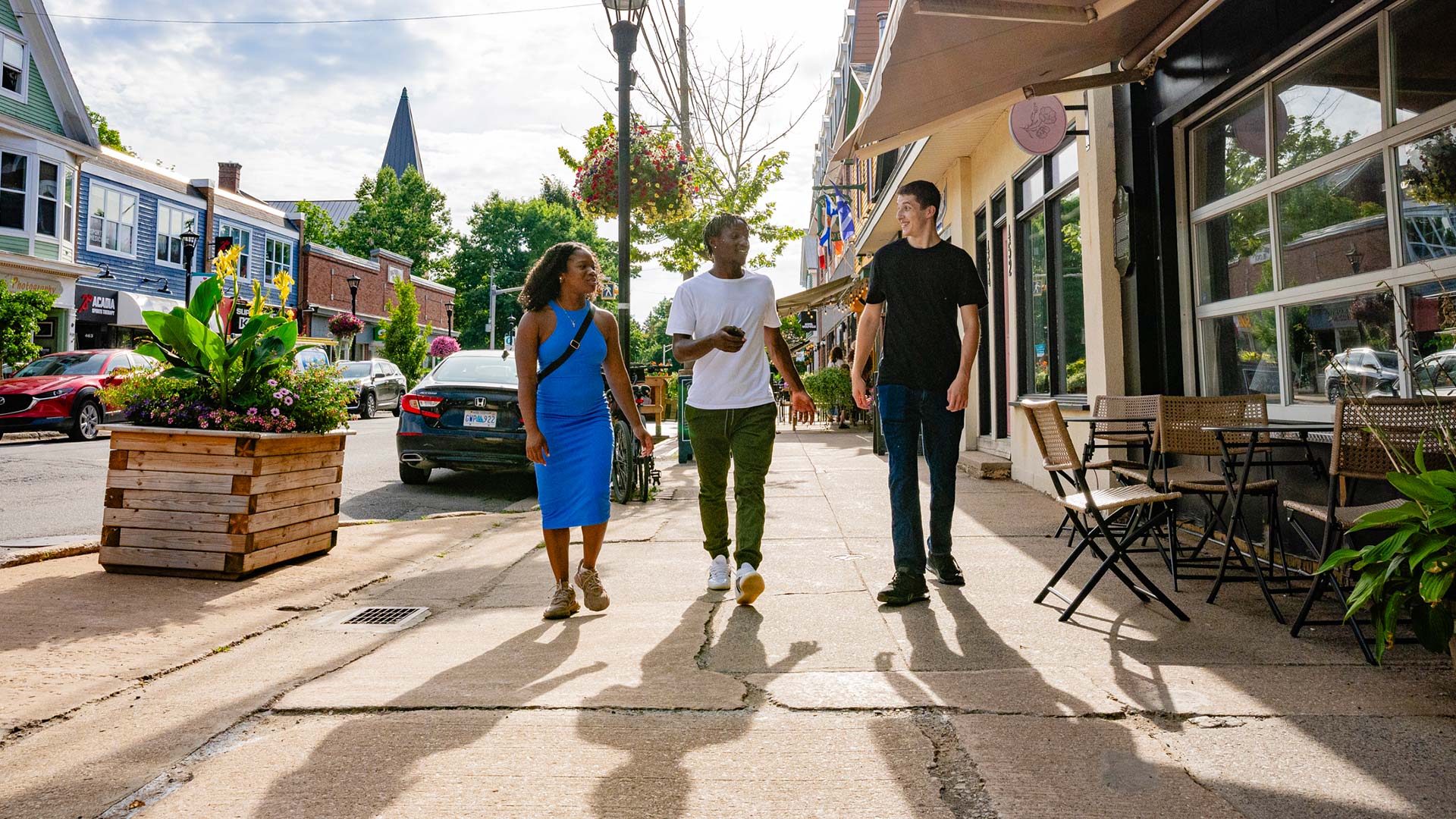 Three students smile as they walk down the sidewalk underneath the neon Acadia Cinema marquee.
