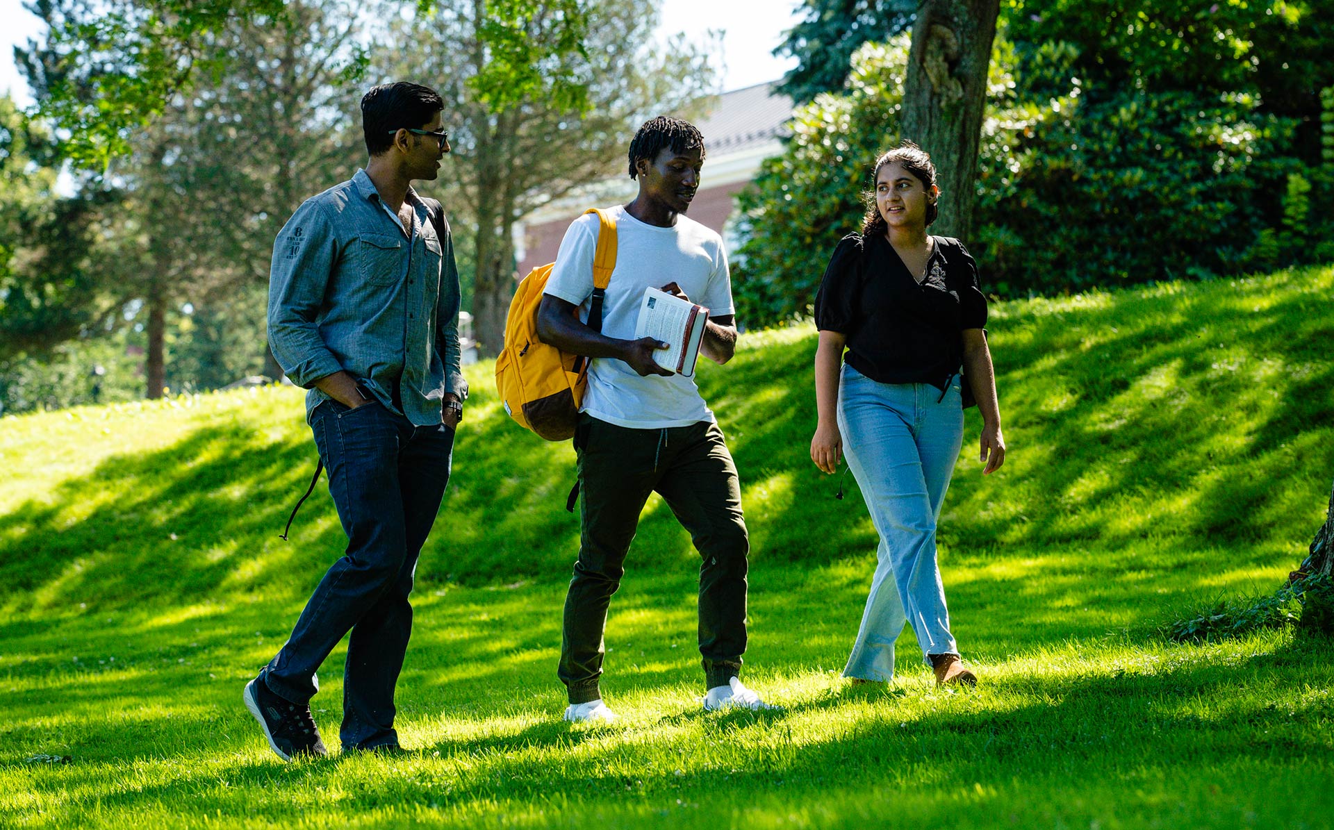 Three students chat as they walk under the trees on the South lawn of campus on the way to class.
